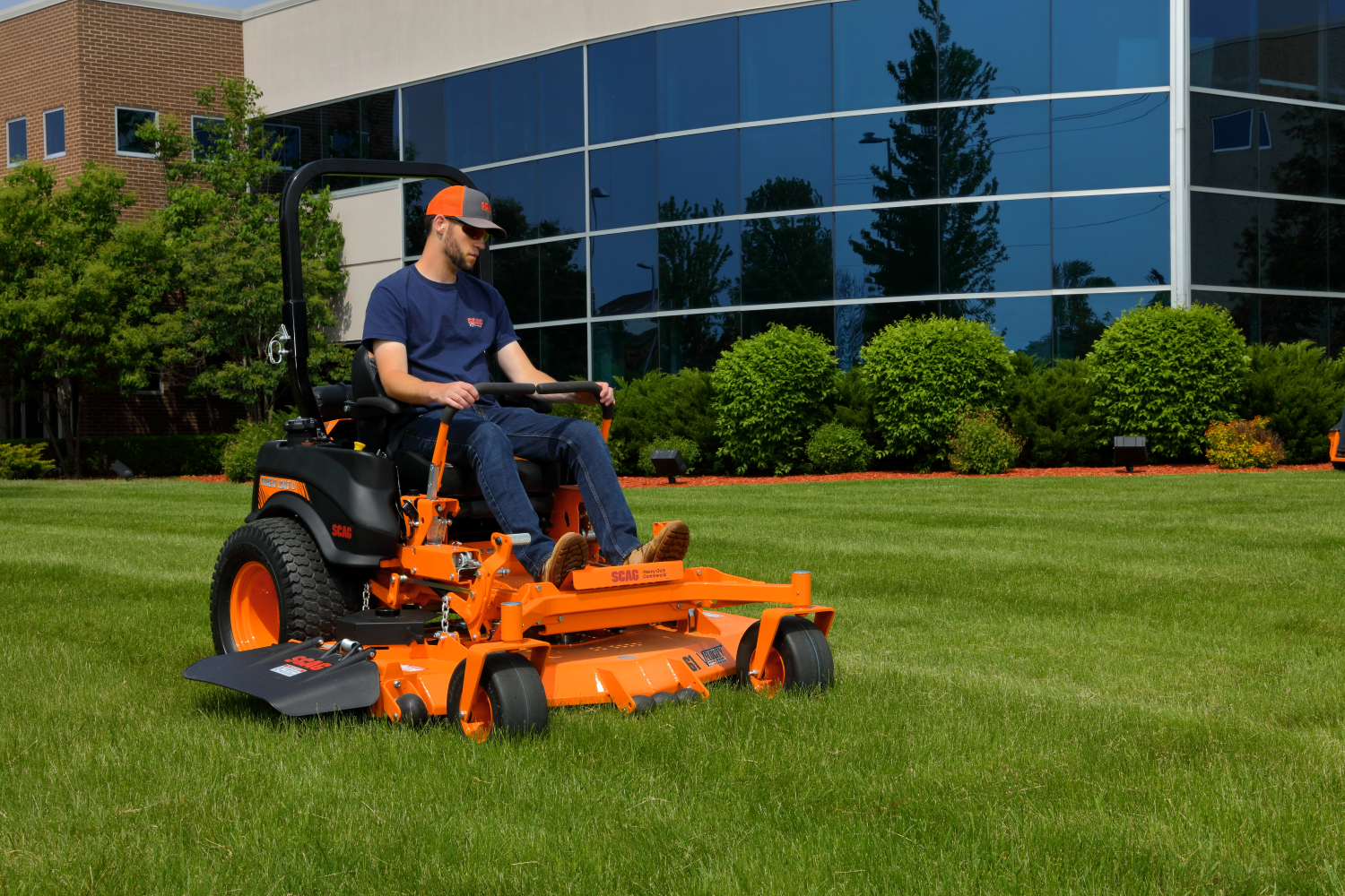 Man on a zero turn riding lawn mower is mowing a lawn outside of a glass office building